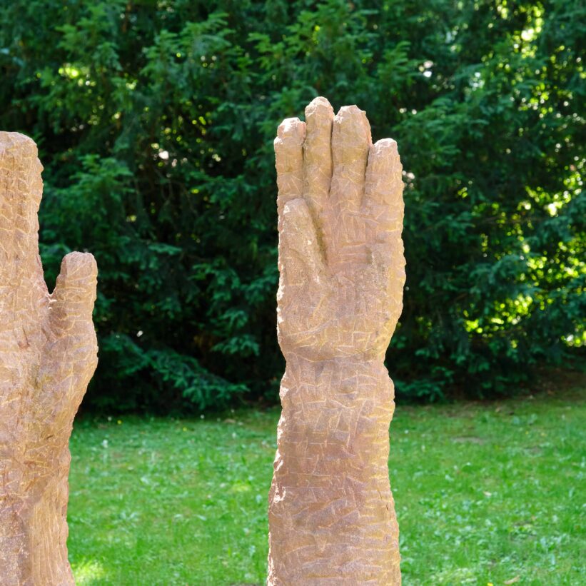 Eine Statue von 2 Stein-Händen ist zu sehen die Richtung Himmel ausgestreckt sind.