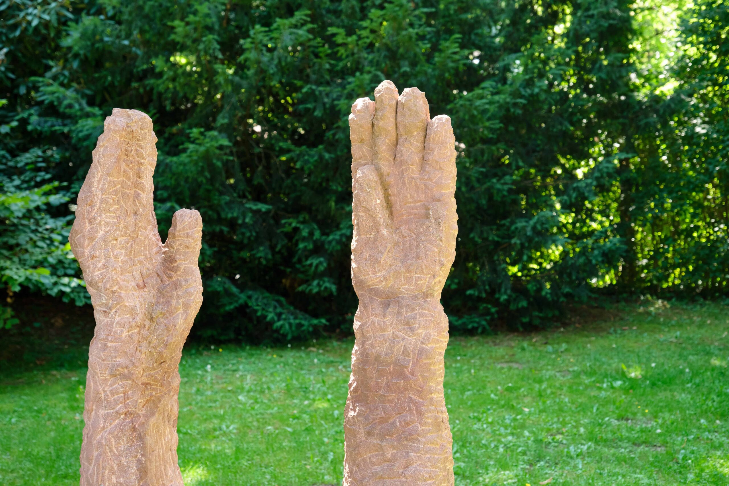 Eine Statue von 2 Stein-Händen ist zu sehen die Richtung Himmel ausgestreckt sind.